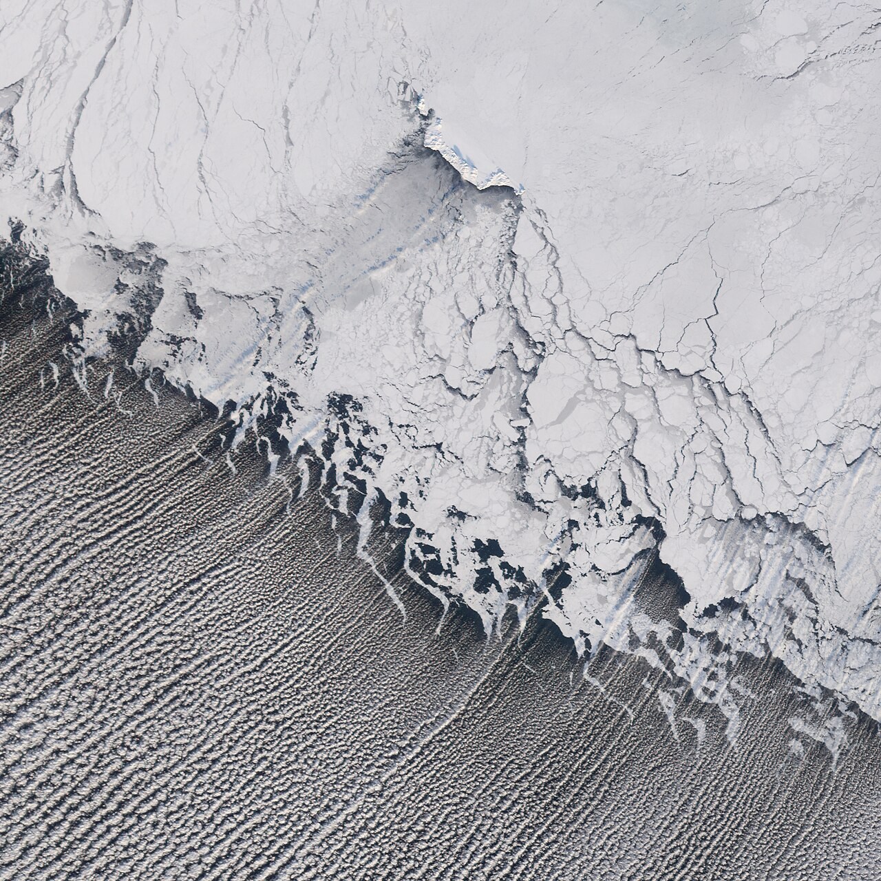 Parallel rows of clouds extend from sea ice across open water in the Bering Sea.