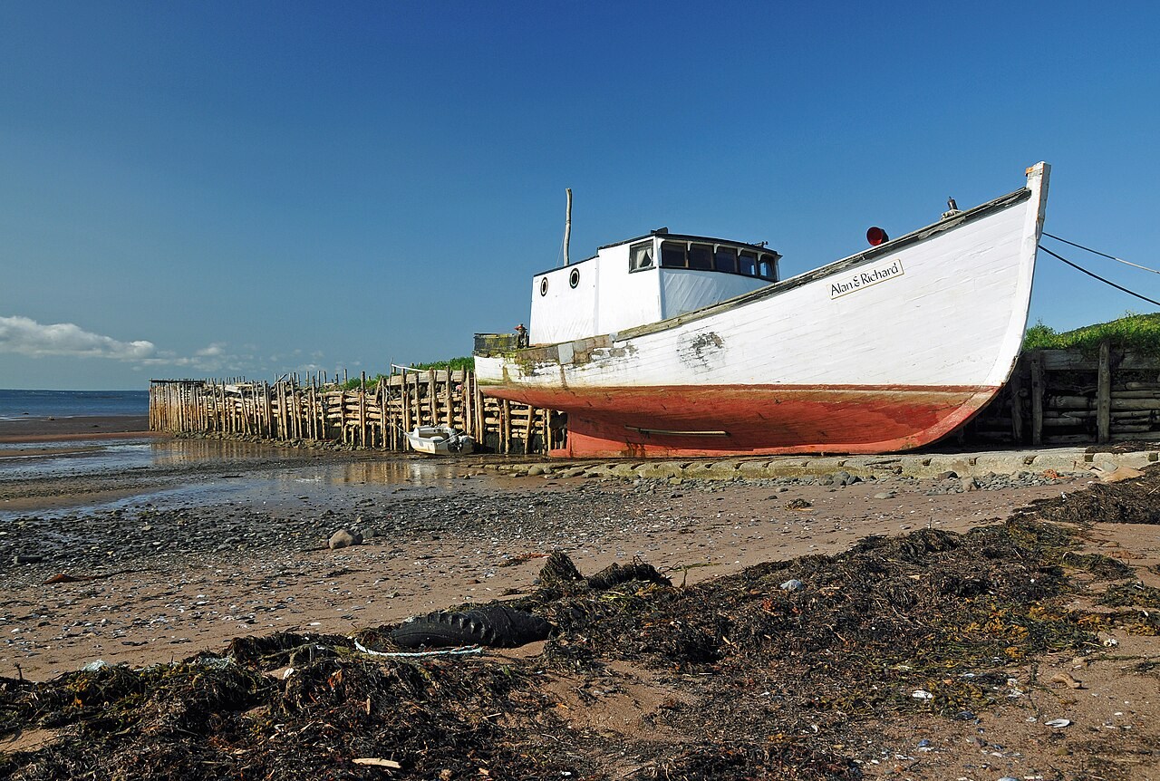 A fishing boat rests on exposed mud beside a wharf at low tide in Nova Scotia.