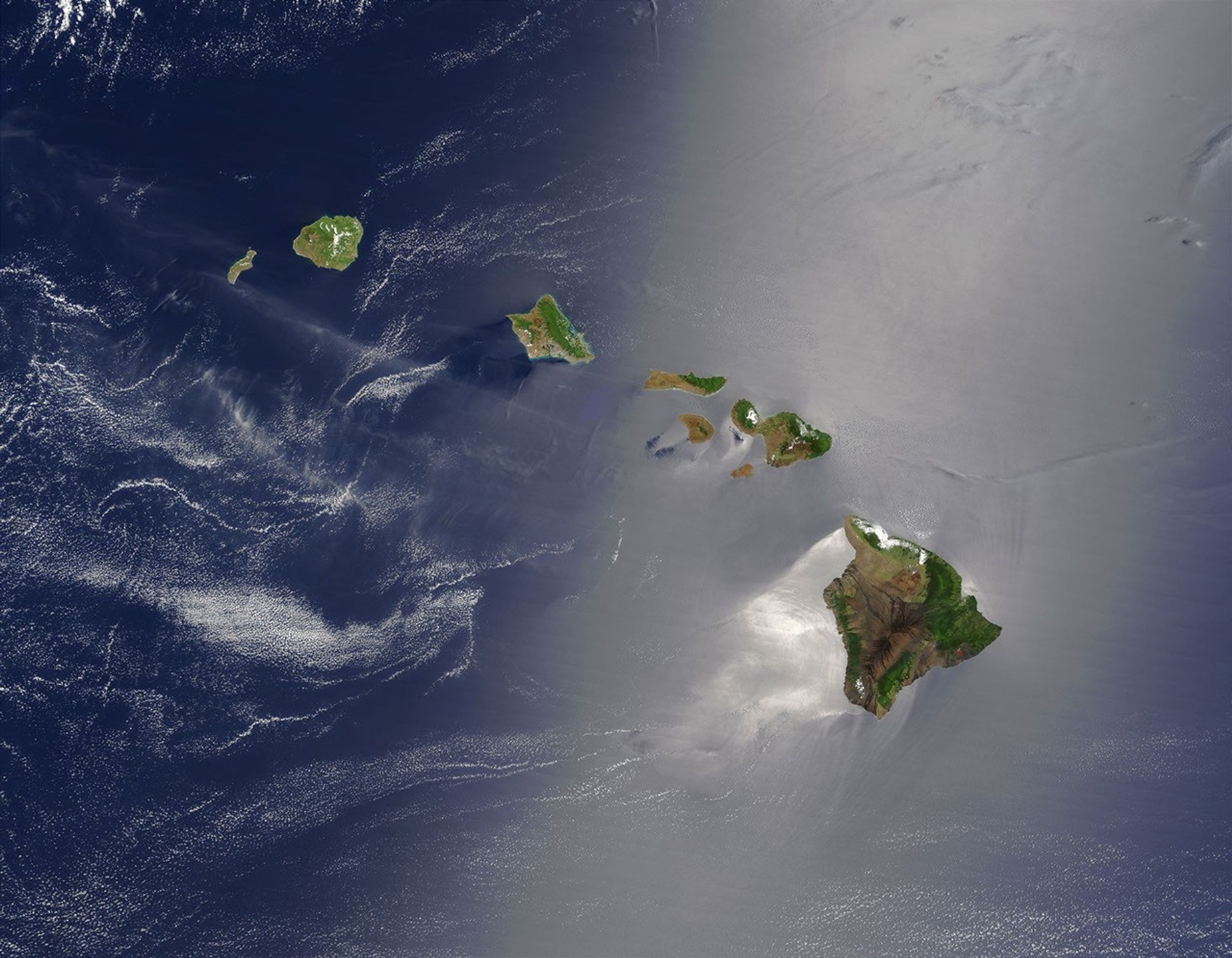 Hawaiian islands with greener windward slopes, drier leeward slopes and silvery sunglint on the Pacific.