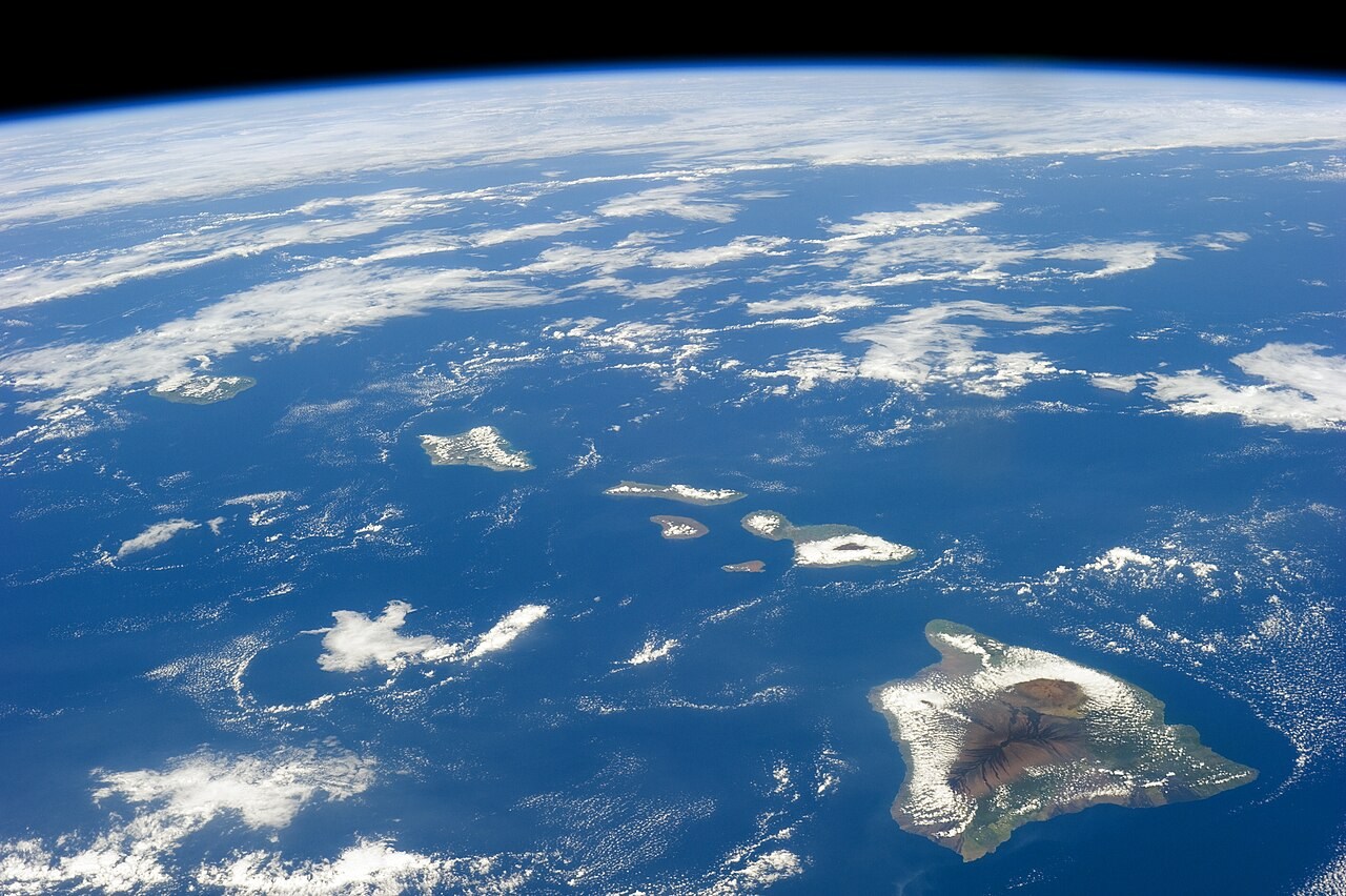The Hawaiian volcanic islands stretch across the Pacific beneath scattered white clouds in an ISS photograph.
