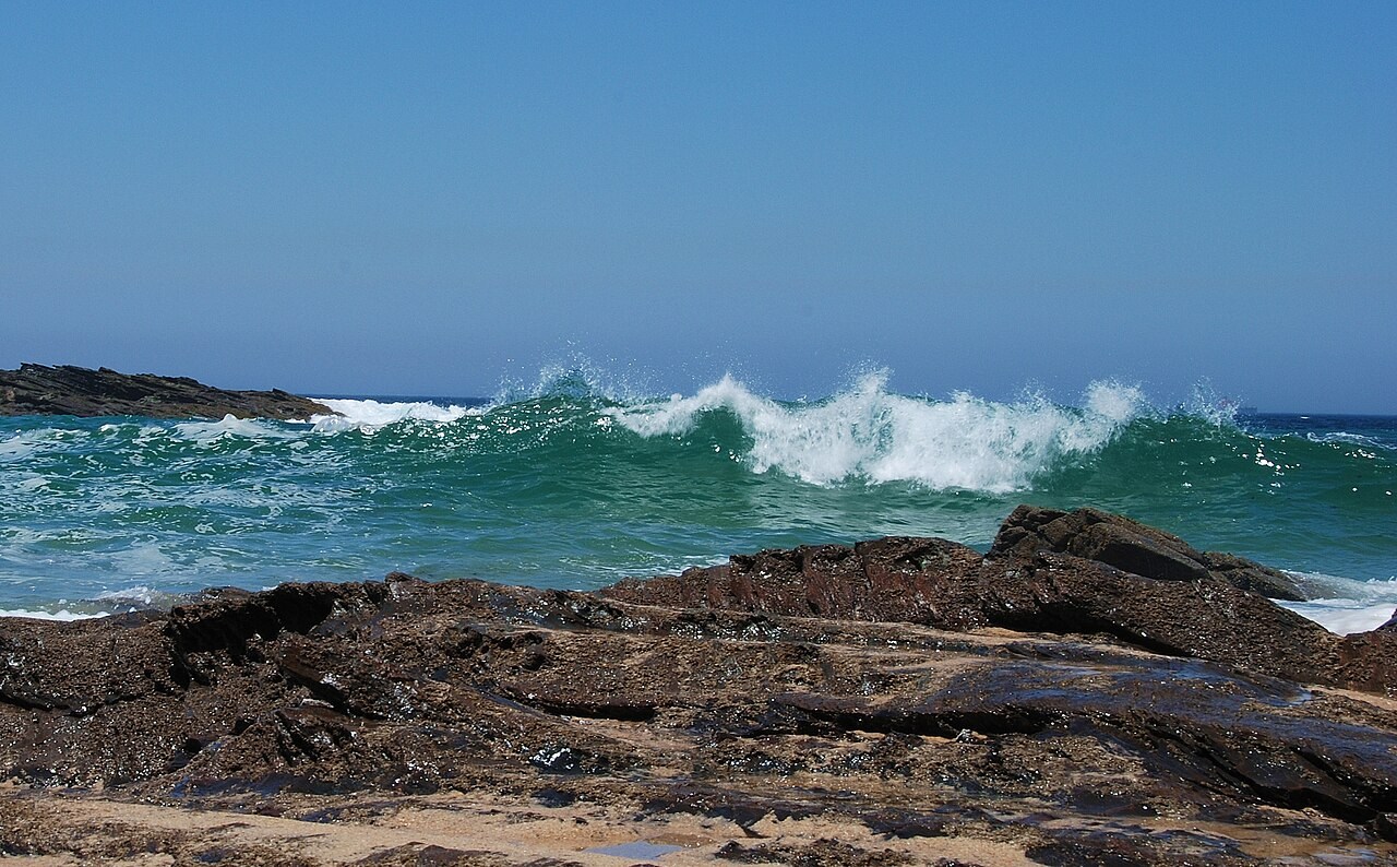 A breaking wave curls and foams along the coast at Porto Covo, Portugal.