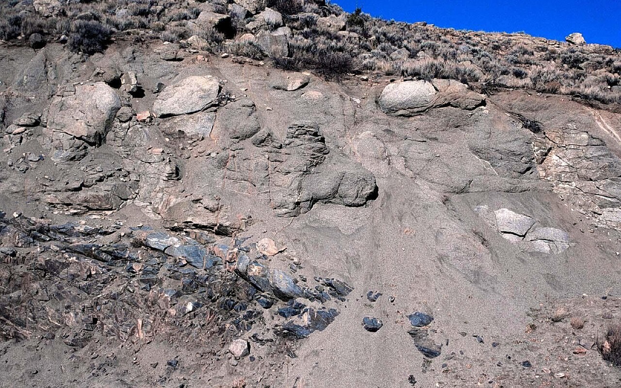 Rounded remnants of granite emerge from loose weathered material in an exposed rock profile.